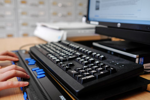 An individual using a Braille keyboard to operate their computer